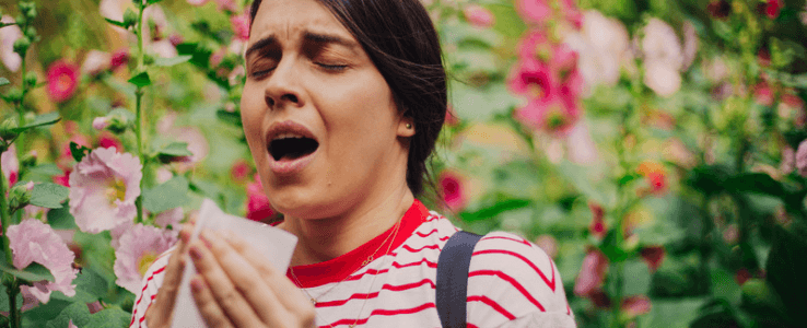 A young woman sneezing in a flower field