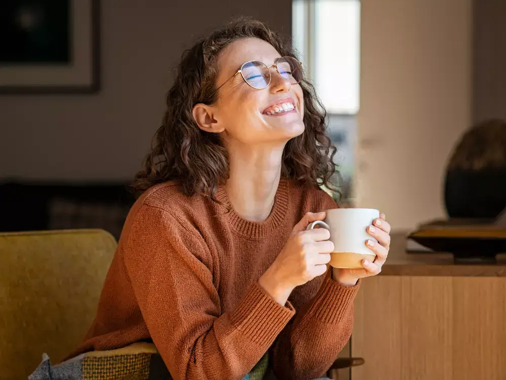 A woman with glasses drinking coffee and smiling