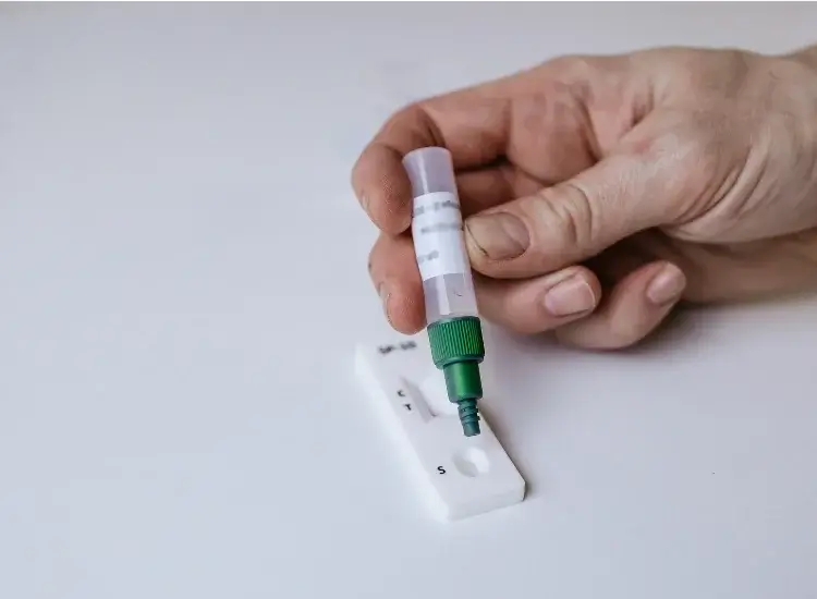 An image of a person squeezing two drops of buffer onto the test cassette